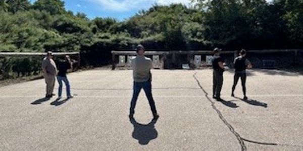 Five people standing at a shooting range with targets in the background.
