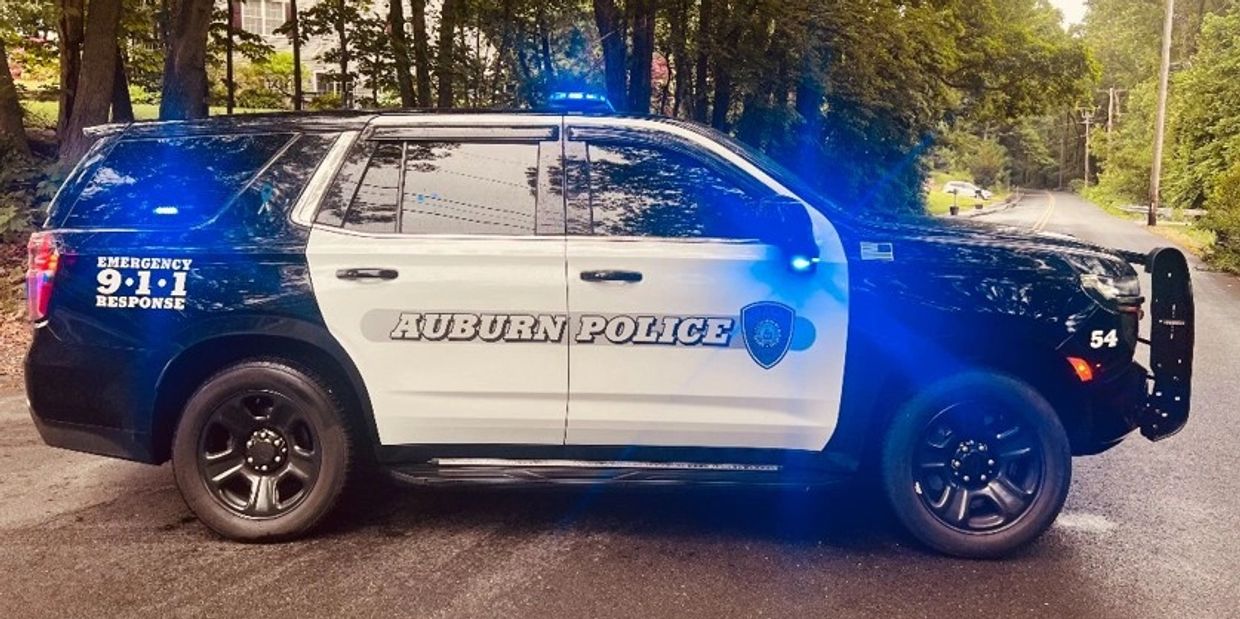 A black and white Auburn Police SUV with flashing blue lights on a tree-lined street.