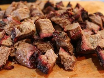 Chopped smoked brisket pieces with a charred crust on a wooden board.
