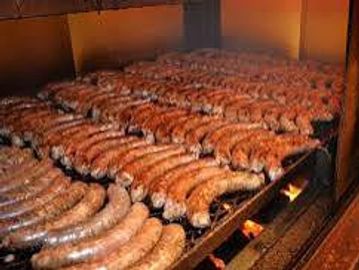 Rows of sausages grilling on a large barbecue grill.