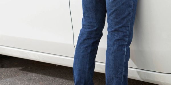 Person standing next to a white car, wearing blue jeans and black shoes.