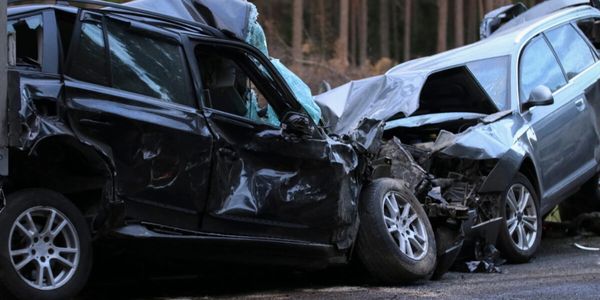 Two heavily damaged cars after a head-on collision on a road.
