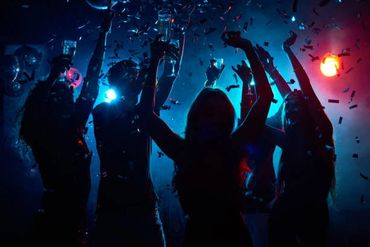 Silhouetted partygoers raise glasses amid confetti and colorful lights.