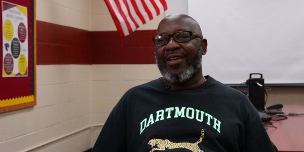 Smiling man wearing a Dartmouth shirt in a classroom setting.