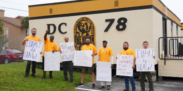 Union workers holding signs supporting UAW strike outside a building.