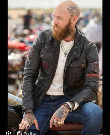 Bearded man with tattoos wearing a leather jacket and sitting on a motorcycle.