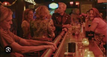 People socializing at a dimly lit bar with drinks and candles.