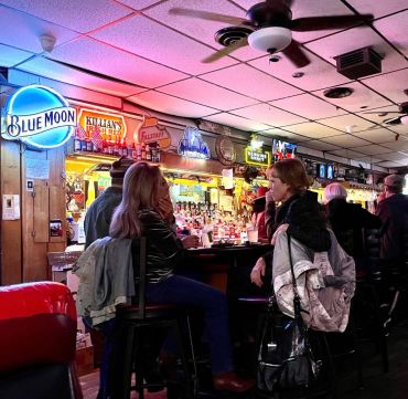People chatting at a cozy bar with neon signs and warm lighting.