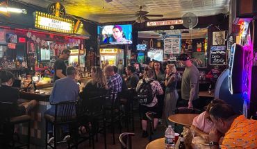 People socializing and enjoying drinks at a cozy, dimly lit bar with neon signs.