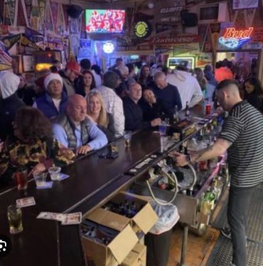 A crowded bar with people enjoying drinks and a bartender serving behind the counter.