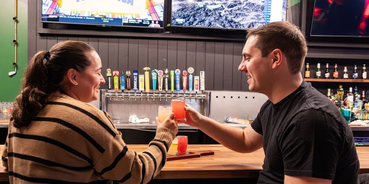 Two people clinking glasses at a bar with beer taps in the background.