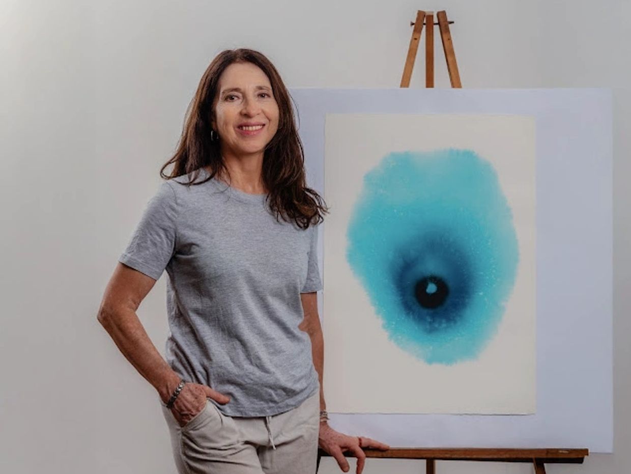 Woman standing beside an abstract blue watercolor painting on an easel.