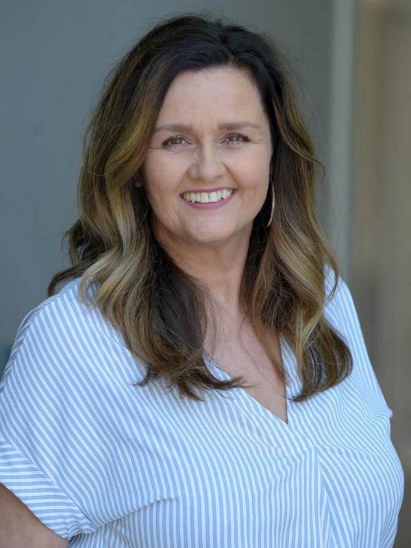 Smiling woman with wavy hair wearing a blue and white striped shirt.