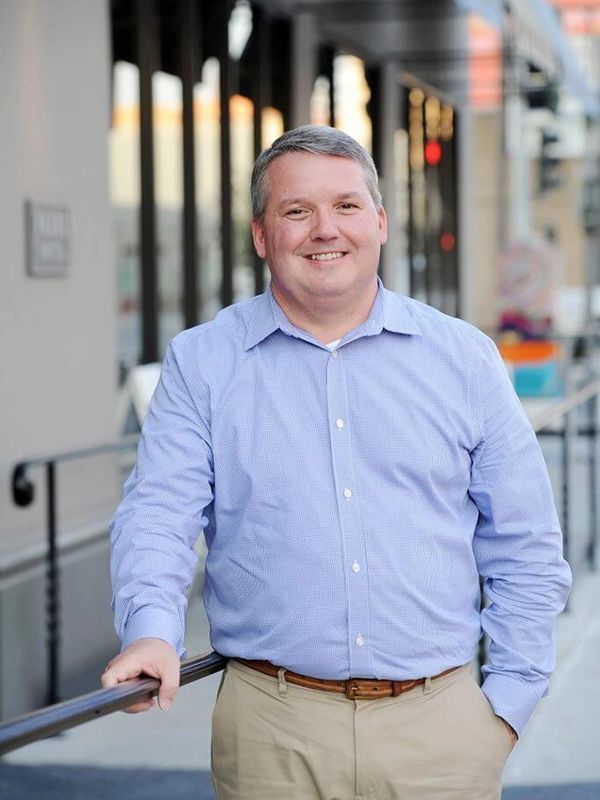 Smiling man in blue shirt and khaki pants outdoors.