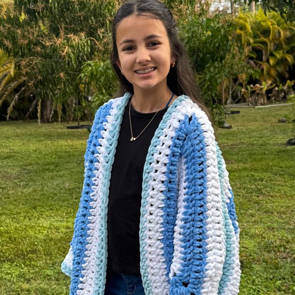 Smiling girl wearing a cozy, handmade blue and white striped crochet cardigan outdoors.