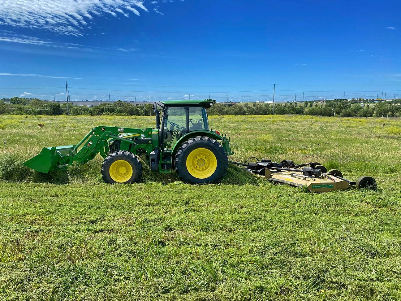 John Deere 5115 M tractor with Land Pride RC2512 12’ bat-wing mower mowing a green field in Nebraska