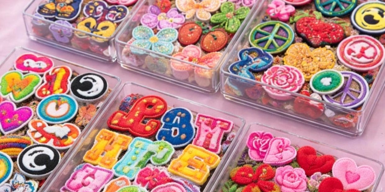 Colorful embroidered patches in clear trays on a pink surface.
