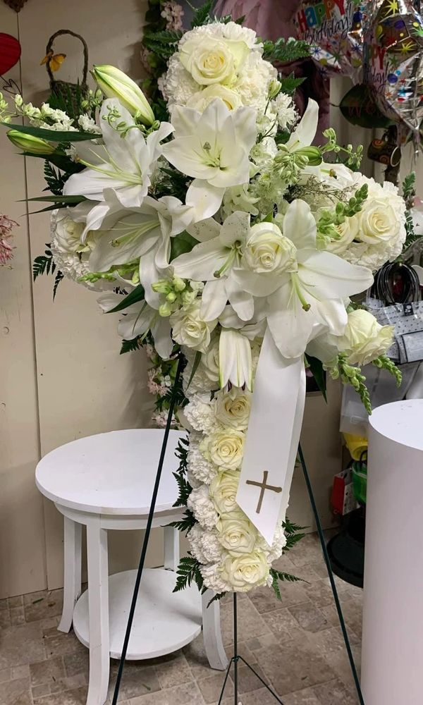 White floral cross arrangement with lilies and roses on a stand.