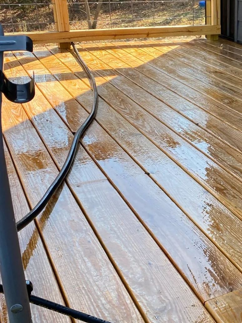Wet wooden deck with a black hose and sunlight casting shadows.