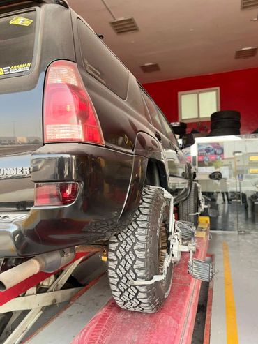Black SUV undergoing tire alignment in a garage.