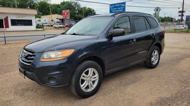Black Hyundai SUV parked on a gravel lot near buildings and signs.