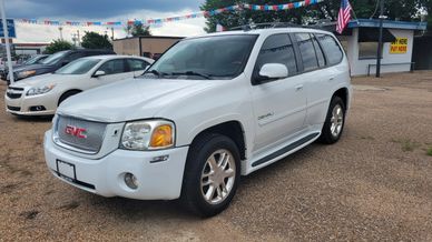 White GMC Envoy SUV parked on a gravel lot with American flag.