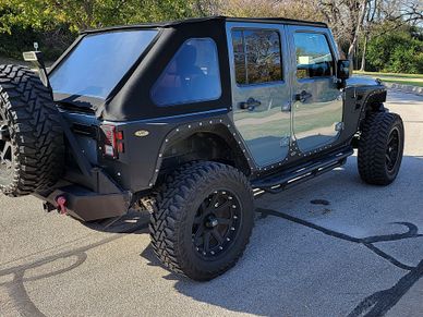 A rugged Jeep Wrangler with large off-road tires parked on pavement.