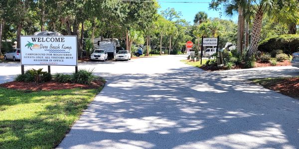 Entrance to a campground with welcome signs and vehicles.