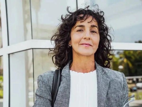 Confident woman with curly hair stands outside a modern building in business attire.