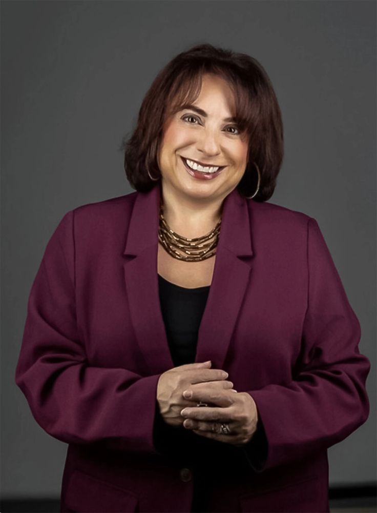 Smiling woman in maroon blazer and gold necklace posing confidently.