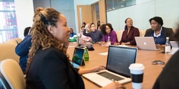 A group of professionals in a meeting room with laptops and coffee.