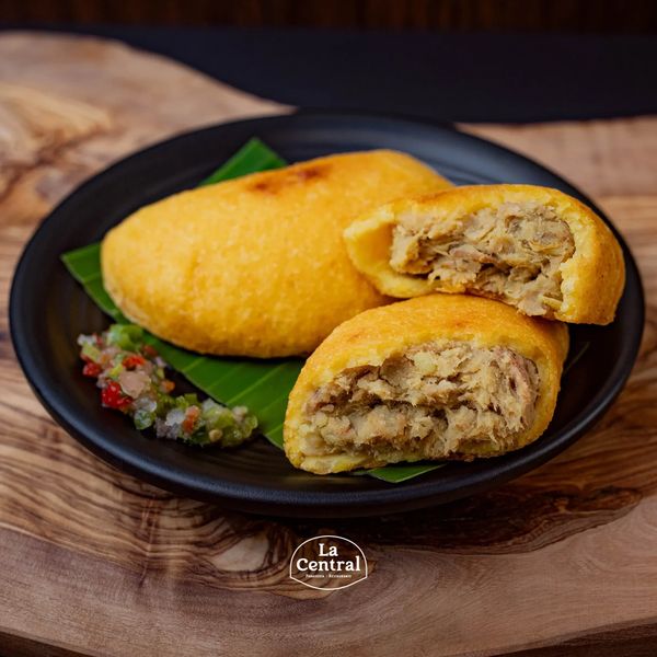 Two stuffed corn empanadas on a black plate with chili sauce and banana leaf.