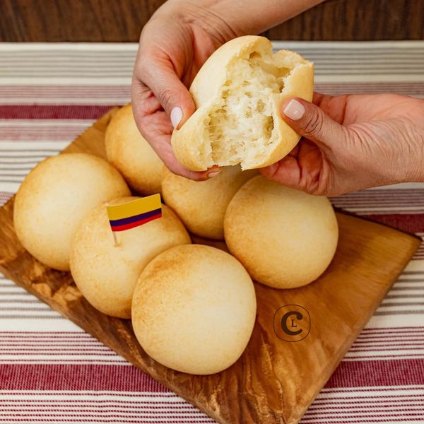 Hands breaking a soft, round bread roll with a Colombian flag on a wooden board.