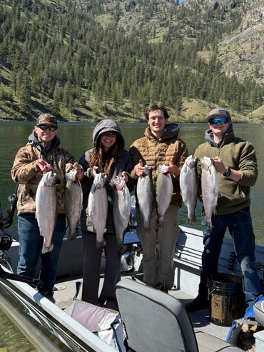 Four people proudly holding large fish on a boat in a lake.