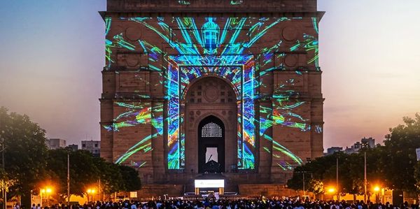 Crowd watching colorful light projections on a large historic monument at dusk.