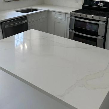 Modern kitchen with white cabinets, marble countertops, and stainless steel appliances.