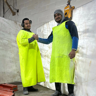 Two workers wearing bright yellow aprons shake hands in an industrial setting.
