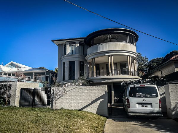Modern two-story house with curved balconies and a parked van.