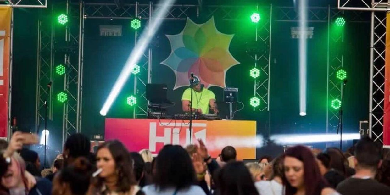 DJ performing on stage with colorful lights at a crowded event.