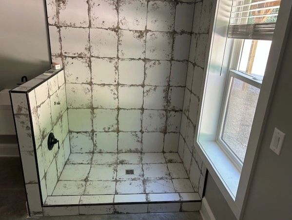 Shower area with dirty, stained white tiles and a nearby window.