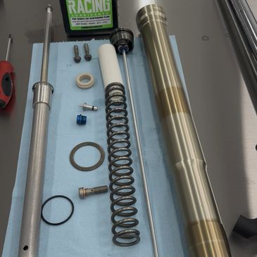 Disassembled motorcycle fork parts with BLUD Racing suspension fluid on a workbench.