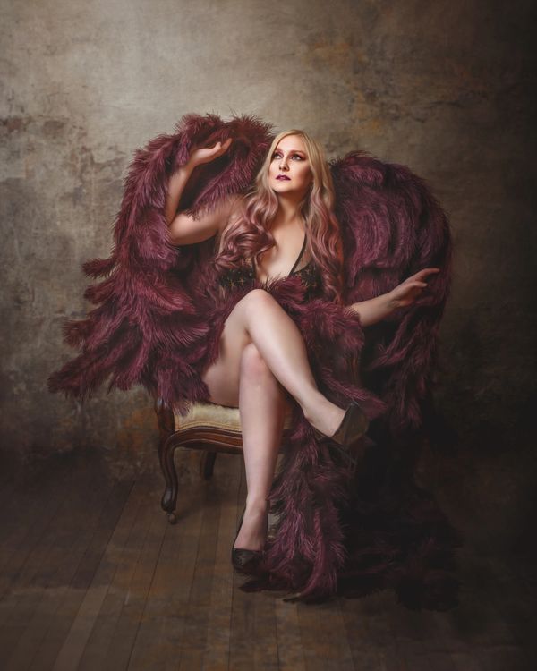 a woman sitting in a chair wearing wine colored angel wings looking up