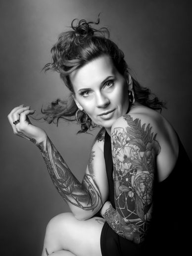 Black and white portrait of a tattooed woman with an intense gaze and tousled hair.