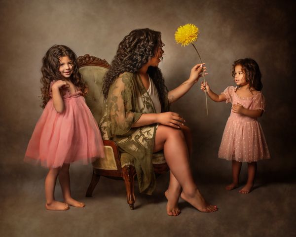 A cute moment of a little girl handing her mom a flower while her sister giggles