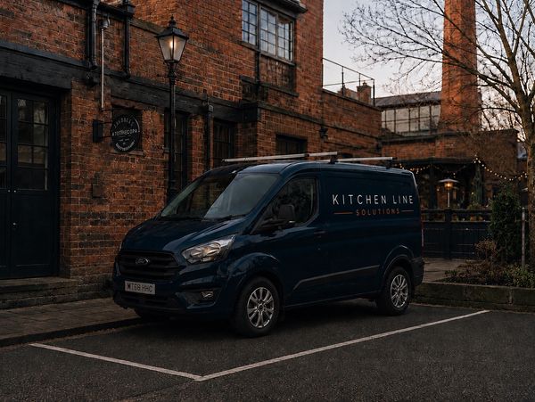 Dark blue Kitchen Line Solutions van parked by a brick building at dusk.