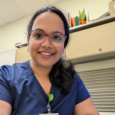 Smiling woman with glasses in blue scrubs.