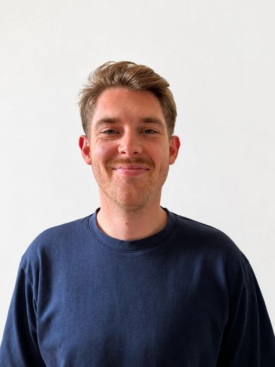 Man met blauwe trui glimlacht naar de camera.