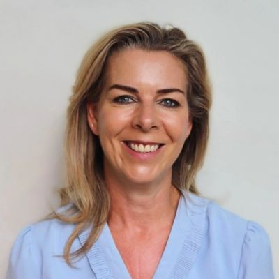 Vrouw met blond haar en een blauwe blouse die glimlacht.