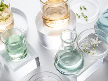 Glass beakers filled with green, amber and clear  liquid with Petri dishes of flowers and leaves.