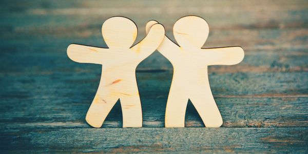 Two wooden figures high fiving or connecting hands